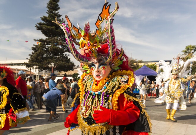 A person in a brightly colored, elaborate costume with a head dress and mask in Chile's Arica’s La Fuerza del Sol festival.