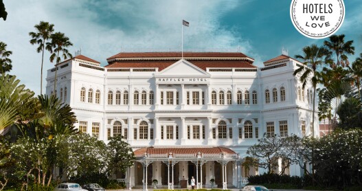 The facade of the Raffles Hotel Singapore has white columns and a red roof.