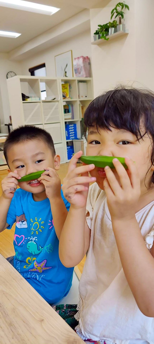 Two children at Olivetree International School in Shibuya-ku, Tokyo, smelling okra and learning about the value of fresh vegetables in the classroom.